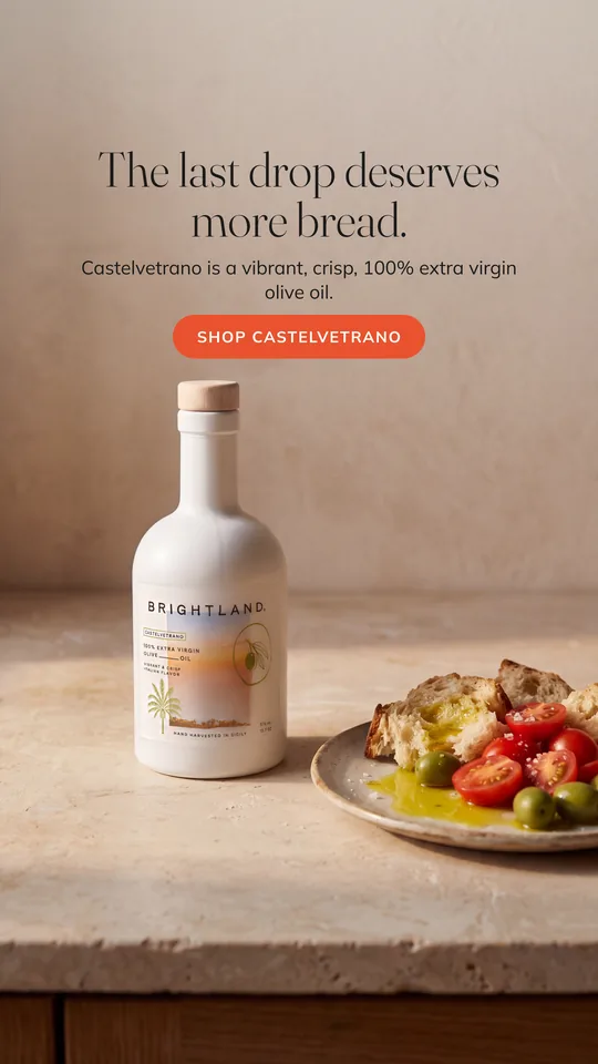 Our concept: the same bottle on a sunlit stone counter beside bread and tomatoes in olive oil.